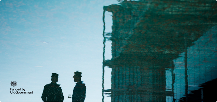 Two people reflected in water beside a UK Government funded mark